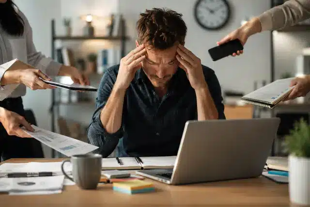 Homme stressé à son bureau, acculé par des mails, appels et téléphones